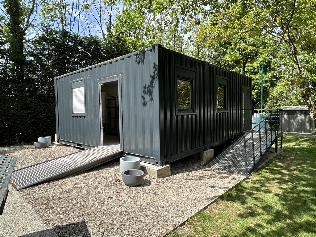 cuisine en container vue de l'exterieur avec une rmape d'accés autour un jardin et une pelouse verte